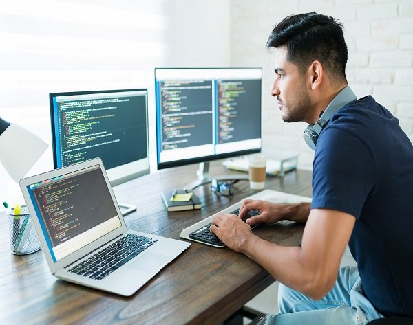 Handsome Young Male Programmer Coding At Desk Side view of attractive Hispanic software developer programming using computer while working from home